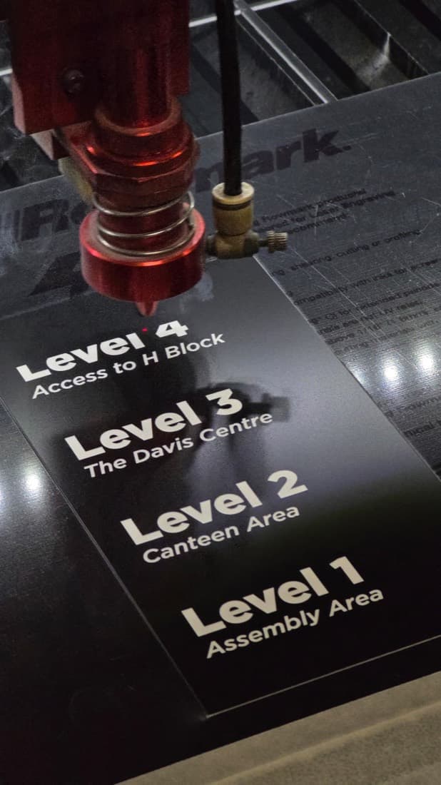 Engraving machine cutting a multi-level building directory and wayfinding sign for a school campus, listing Level 1 Assembly Area through Level 4 H Block