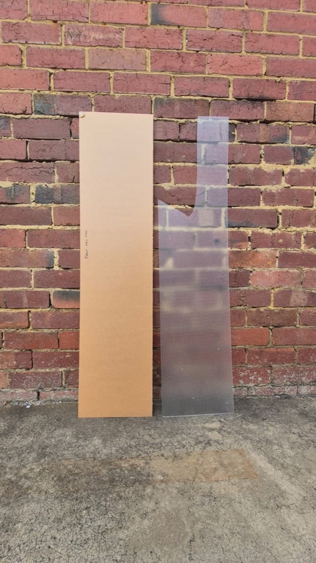 Clear textured polycarbonate glazing sheet leaning against a brick wall alongside its protective packaging