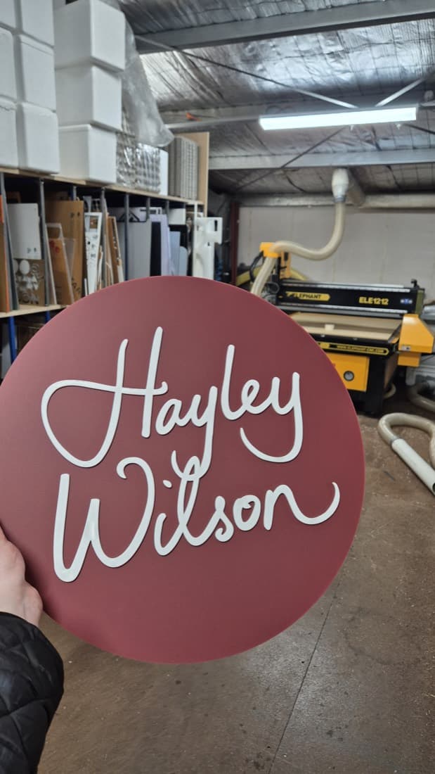 Round routed acrylic Hayley Wilson business sign held in the workshop